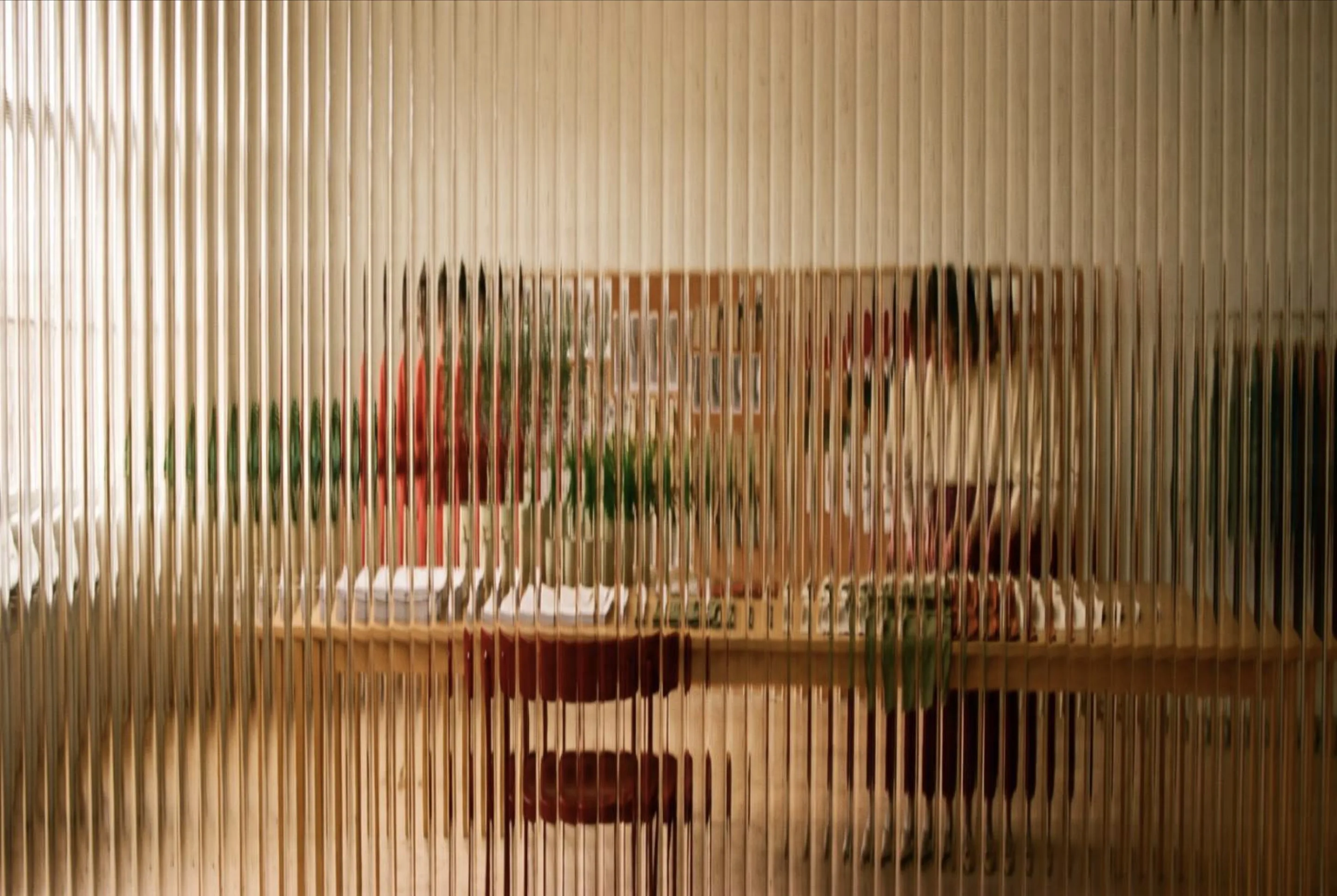 A studio seen through ribbed glass: people at a long table, plants and warm light, all softened into vertical bands.